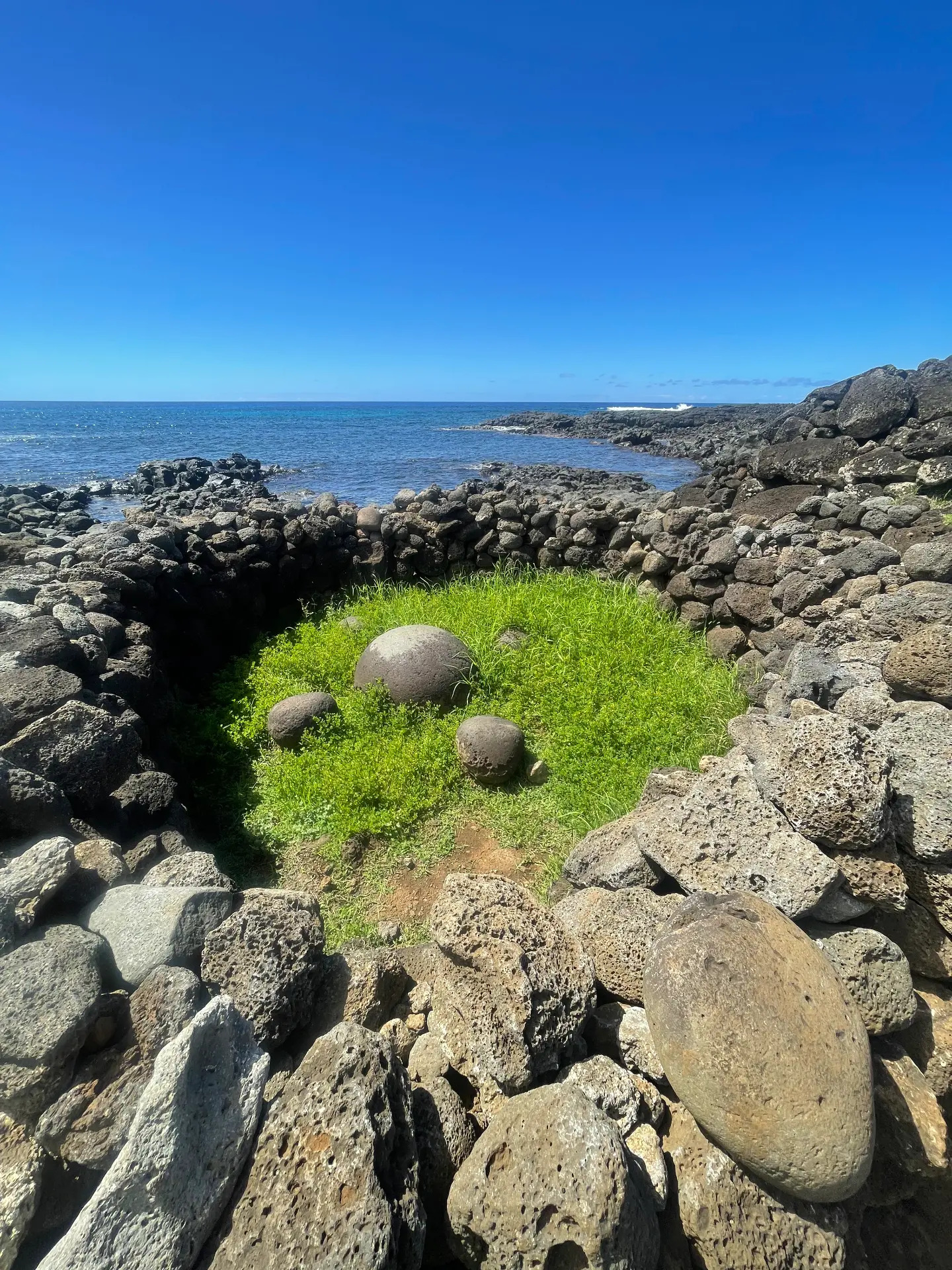 The round stone of Te Pito Kura inside a curved stone wall by the sea